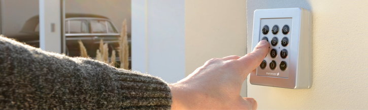 Eine Hand mit grauem Pullover bedient einen silbernen Funk-Codetaster zur Torsteuerung.